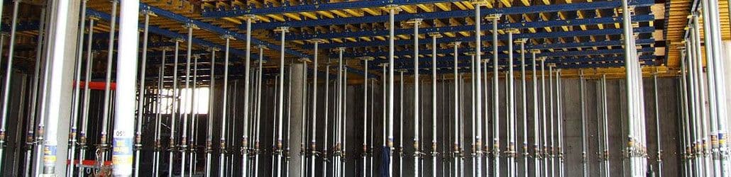 Rij stempels of schoorpalen die een bekisting ondersteunen tijdens de bouw van een betonnen plafond. De stempels staan gelijkmatig verspreid onder houten en metalen liggers.