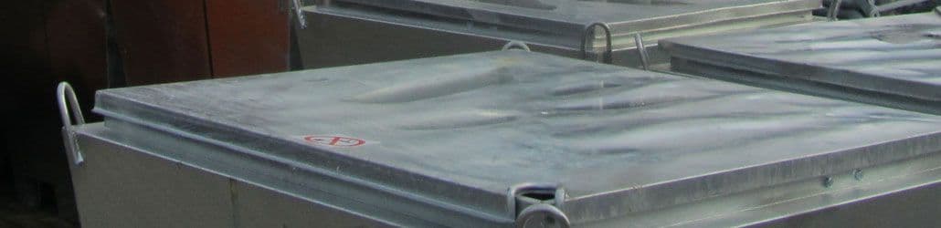 Close-up van verzinkte bouwwaterputten met metalen deksels en hijsogen, gestapeld op een bouwplaats.