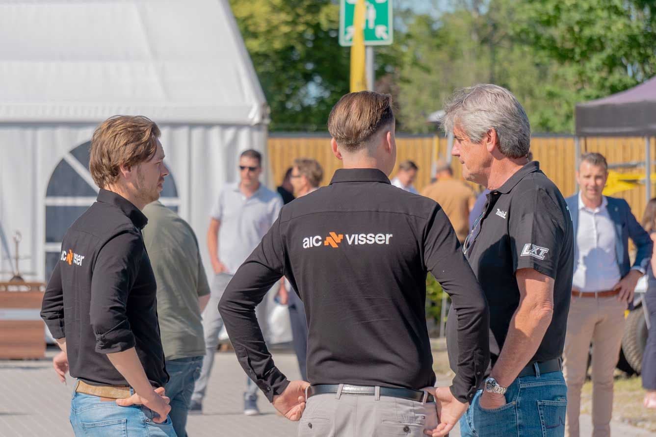 Drie mannen in zwarte bedrijfsshirts praten buiten tijdens een evenement.