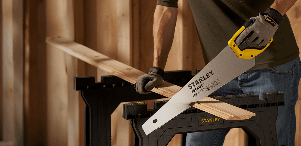 Persoon zaagt houten plank met Stanley handzaag op zaagbok.