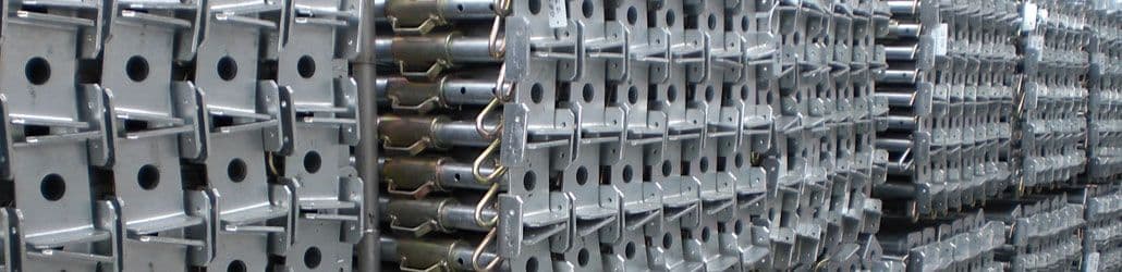 Grote voorraad metalen bouwstempels met verstelbare koppen, gestapeld en klaar voor gebruik op de bouwplaats.