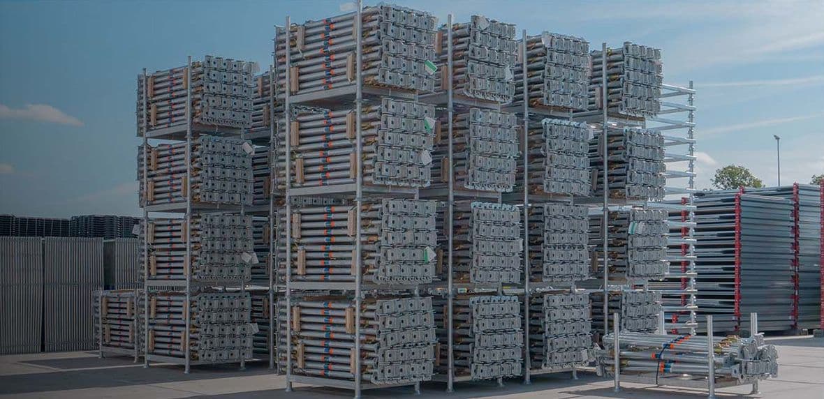 Grote gestapelde rekken met bouwstempels op een buitenterrein onder helder weer.