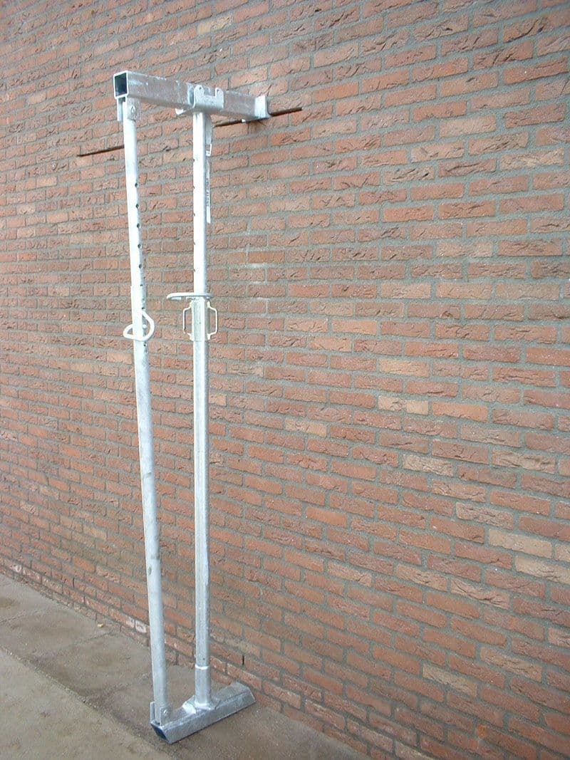 Volledig gemonteerde Stutalone gevelstempel tegen een bakstenen muur, gebruikt voor het tijdelijk ondersteunen van metselwerk tijdens gevelrenovatie of -bouw.