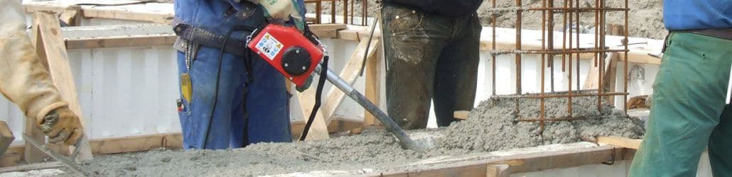 Bouwvakkers gebruiken een betontrilnaald om vers gestort beton te verdichten in een bekisting met wapeningsstaal.