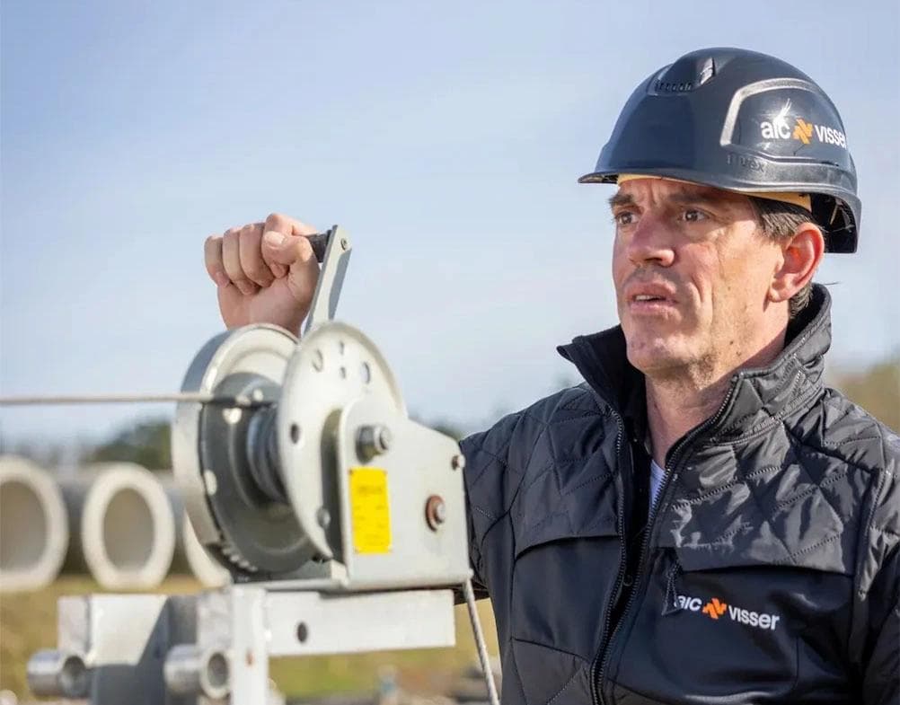 Persoon met veiligheidshelm bedient een handlier op een bouwterrein.
