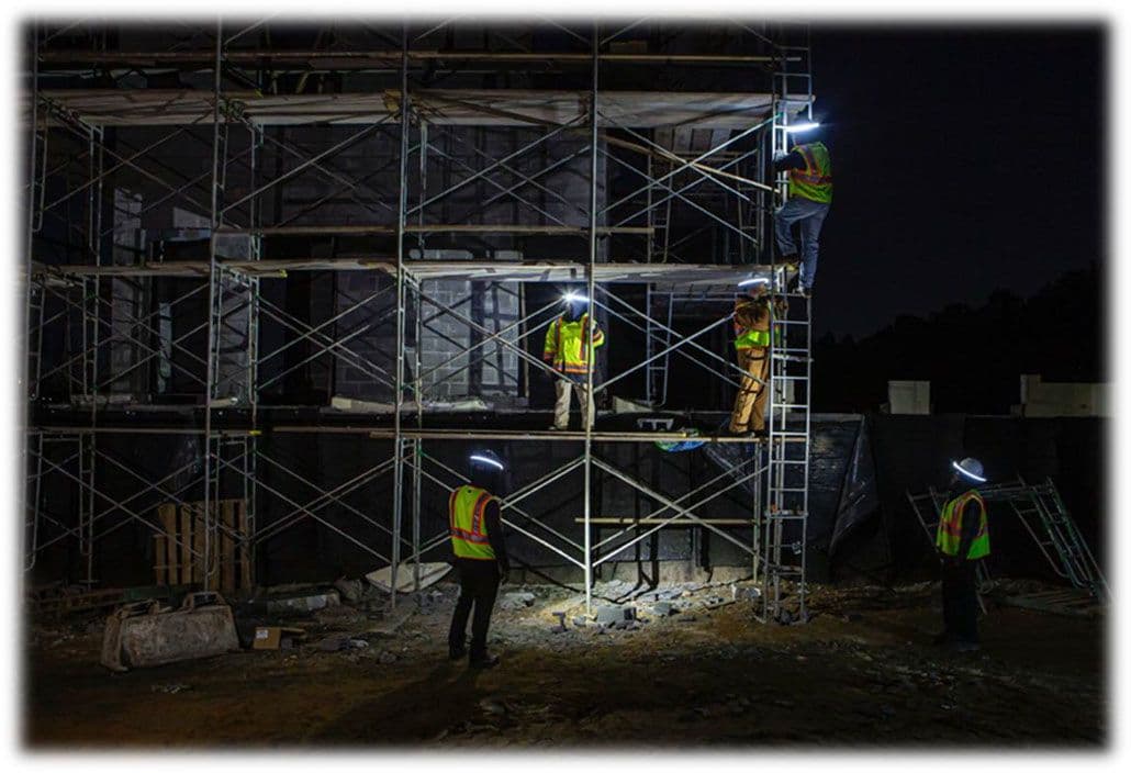 Bouwvakkers werken 's nachts op een steiger, uitgerust met helmlampen en reflecterende veiligheidsvesten. De verlichting van de helmlampen verlicht hun directe werkomgeving.