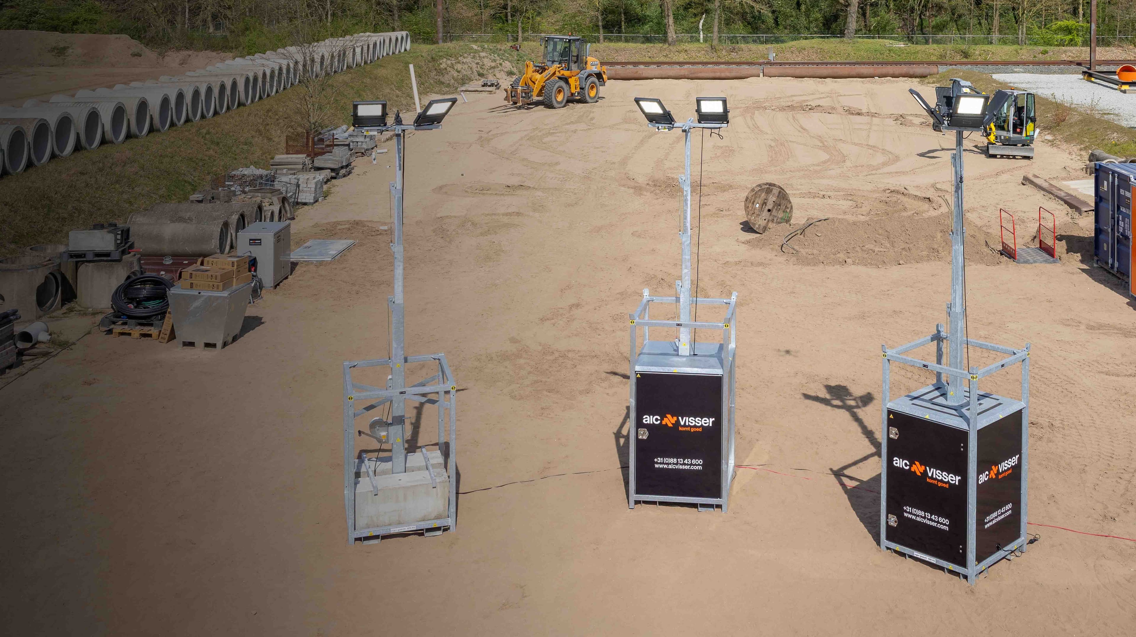 Bouwplaats met graafmachines, containers en gestapelde betonnen buizen op zandterrein.