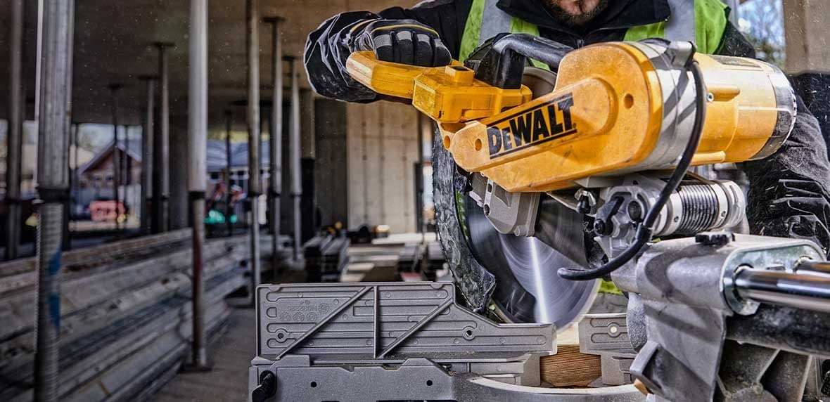 Bouwvakker zaagt houten plank met gele DeWalt-cirkelzaag op een bouwplaats.