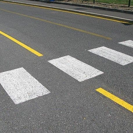 Geverfde witte zebrapadstrepen en gele rijstrookmarkeringen op een asfaltweg, gemarkeerd met lijnmarkeringsverf.