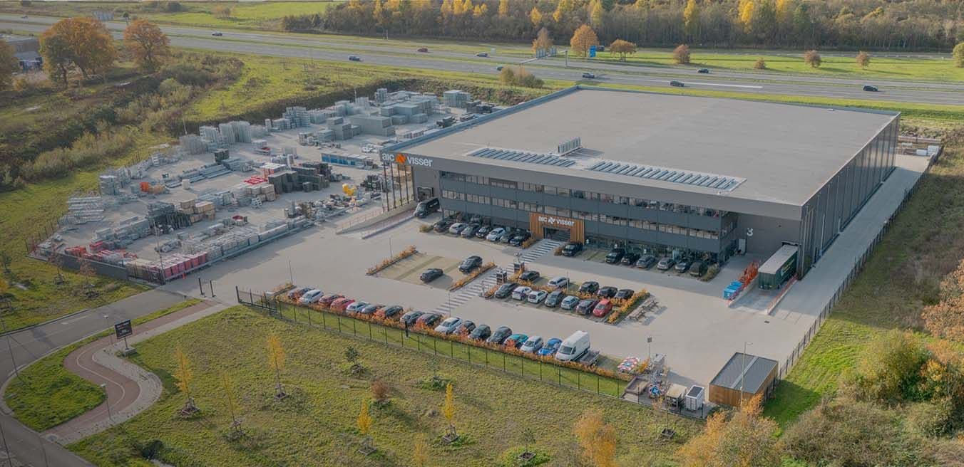 Luchtfoto van het AIC Visser bedrijfsterrein in Assen met opslagrekken, tenten en een bedrijfsgebouw naast de snelweg.
