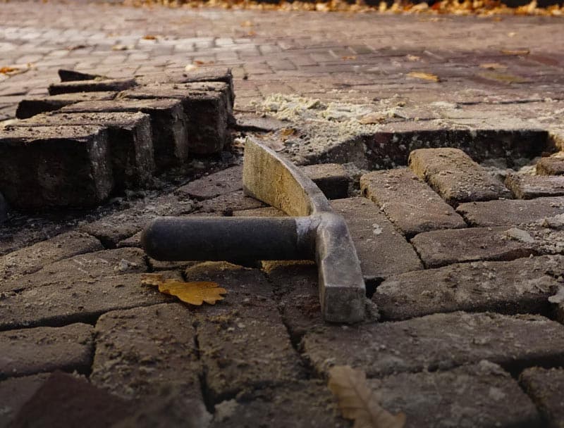 Straathamer ligt op opgebroken klinkers met losse stenen en herfstbladeren eromheen.