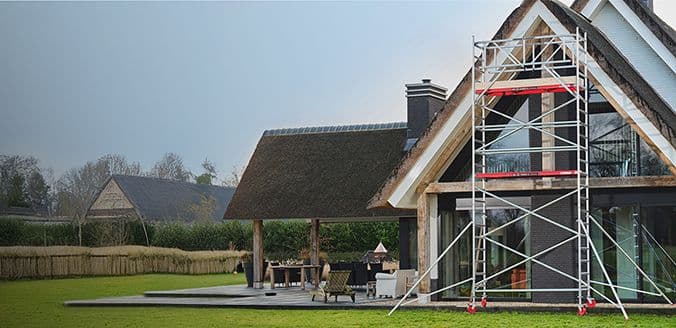 Stalen rolsteiger voor een rietgedekt huis met grote ramen in een groene tuin.