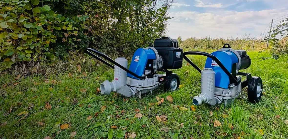 Blauwe AMT-waterpomp op modderige bouwplaats met graafmachine op de achtergrond.