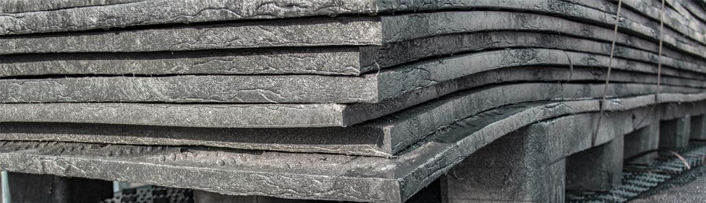 Close-up van gestapelde kunststof rijplaten op pallets, met zichtbare textuur en lichte vervorming door gewicht of opslag.