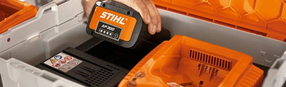 Close-up van een STIHL AP 300 accu die in een oranje acculader wordt geplaatst, opgeborgen in een stevige kunststof opbergkoffer met vakken voor veilig transport en opslag.