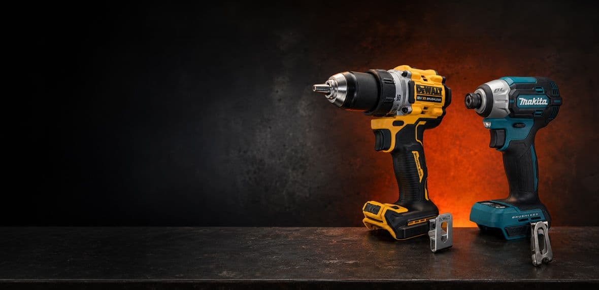 Gele DeWalt-boormachine en blauwgroene Makita-slagschroevendraaier op donkere werkbank.