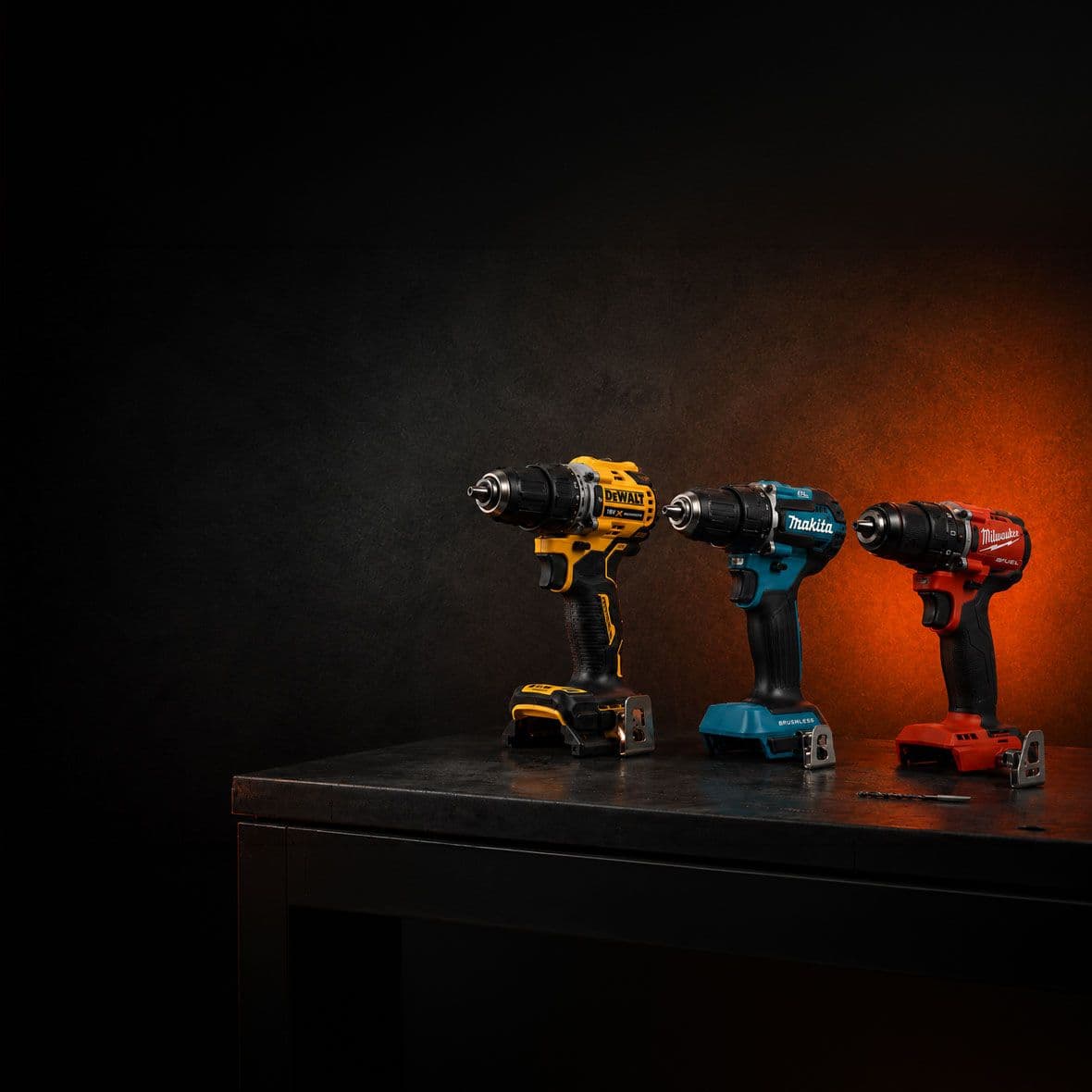 DeWalt, Makita, Milwaukee boormachines op een tafel met zwart oranje achtergrond