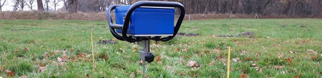 Handpenetrometer geplaatst in een grasveld met markeerstokken, gebruikt voor het meten van bodemverdichting of draagkracht op locatie.