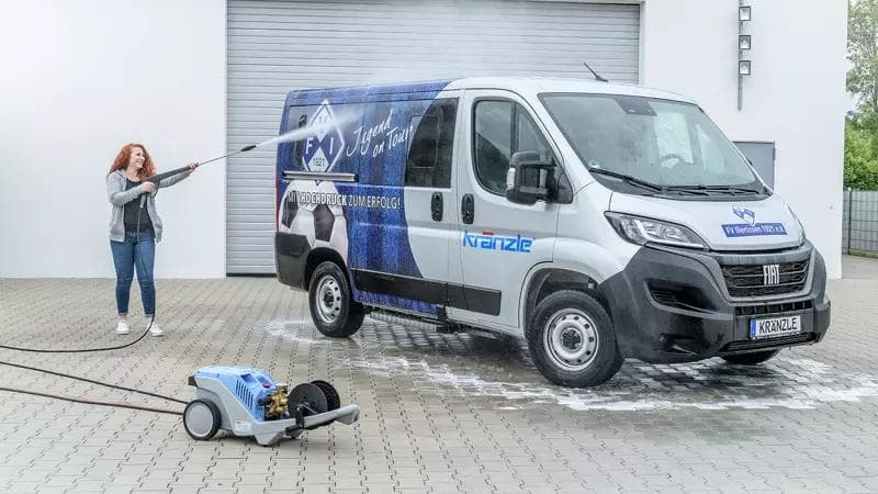 Vrouw met heel mooie, lange, rode krullen spuit met een Kränzle hogedrukreiniger een bestelbus schoon