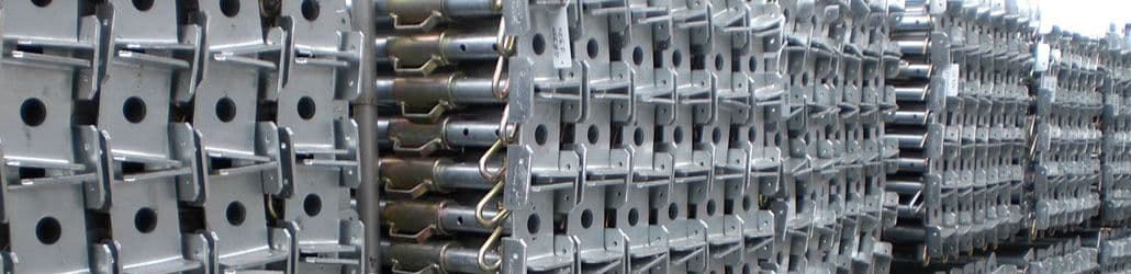 Grote stapel metalen stempels of schoren, opgestapeld in rijen, klaar voor gebruik op een bouwplaats. De stempels zijn thermisch verzinkt en voorzien van verstelmechanismen.